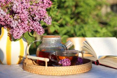 Bahçedeki masada güzel leylak çiçekleri, çay ve kitap, yakın plan.