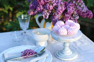 Güzel leylak çiçekleri, zephyrler, tabaklar, çatal bıçak takımı, bardaklar ve bahçede yanan mum.