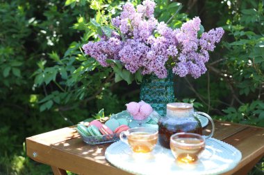 Vazoda güzel leylak çiçekleri, bahçedeki ahşap masada tatlı ve çay.