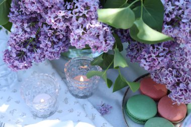 Güzel leylak çiçekleri, tatlılar ve yanan mumlar bahçede, manzaranın üstünde.