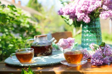 Bahçedeki ahşap masada güzel leylak çiçekleri, çay ve zephyrler.