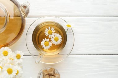 Fincanda nefis papatya çayı, esmer şeker, çaydanlık ve beyaz ahşap masada taze çiçekler, düz yatak. Metin için boşluk