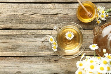 Cam bardakta nefis papatya çayı, taze çiçekler, ahşap masada bal ve çaydanlık, düz yatak. Metin için boşluk