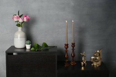 Zarif şamdanlar yanan mumlar vazoda laleler ve gri duvarın yanındaki dolapta diğer dekorlar.