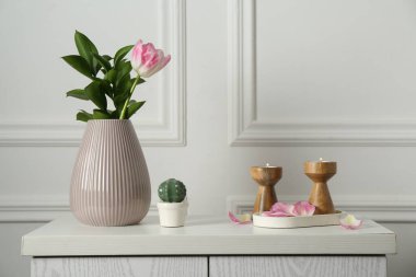 Zarif şamdanlar, yanan mumlar, vazoda lale ve beyaz duvarın yanındaki dolapta diğer dekorlar.