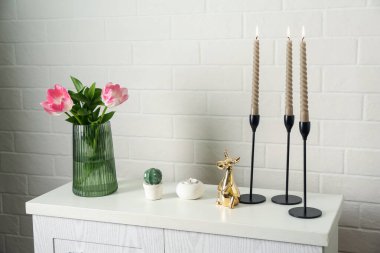 Yanan mumları olan zarif şamdanlar vazoda laleler ve beyaz tuğla duvarın yanındaki şifoniyerde diğer dekorlar.
