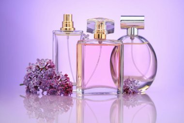 Ayna yüzeyinde mor arkaplana karşı parfüm şişeleri ve leylak çiçekleri