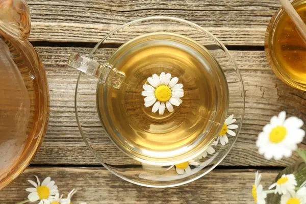 Cam bardakta nefis papatya çayı, taze çiçekler, bal ve çaydanlık ahşap masada, düz uzanmış