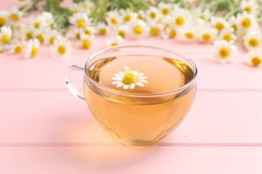 Cam bardakta nefis papatya çayı ve pembe ahşap masada taze çiçekler, yakın plan.