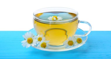 Cam fincanda nefis papatya çayı ve beyaz arka planda açık mavi ahşap masada taze çiçekler.