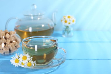 Cam bardakta nefis papatya çayı, taze çiçekler ve açık mavi ahşap masada kahverengi şeker, yakın plan. Metin için boşluk