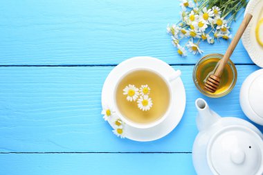 Fincanda nefis papatya çayı, taze çiçekler ve açık mavi ahşap masada bal, düz yatak. Metin için boşluk
