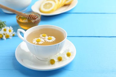 Fincanda nefis papatya çayı, taze çiçekler, açık mavi ahşap masada limon ve bal, yakın plan. Metin için boşluk