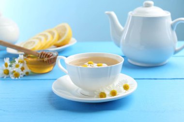 Lezzetli papatya çayı, taze çiçekler, limon ve bal açık mavi ahşap masada, yakın plan.