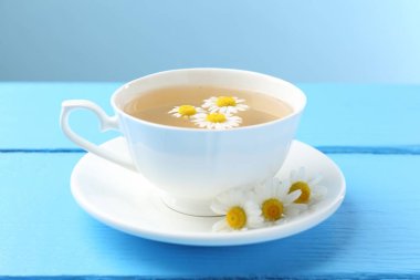 Fincanda nefis papatya çayı ve açık mavi ahşap masada taze çiçekler, yakın plan.