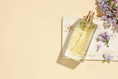 Bir şişe parfüm ve soluk sarı arka planda güzel leylak çiçekleri. Metin için boşluk