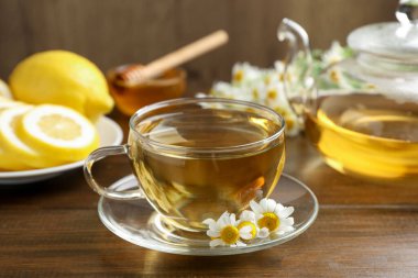 Cam bardakta nefis papatya çayı, taze çiçekler, ahşap masada limon ve bal, yakın plan.