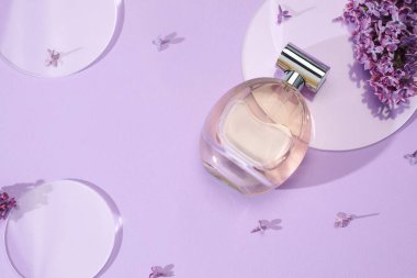 Bir şişe parfüm ve açık mor arka planda güzel leylak çiçekleri.