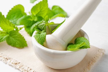 Taze limon merhemi yaprakları ve beyaz ahşap masada havan topuzu, yakın plan.