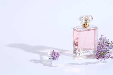 Açık gri arka planda bir şişe parfüm ve leylak çiçeği, yakın plan. Metin için boşluk