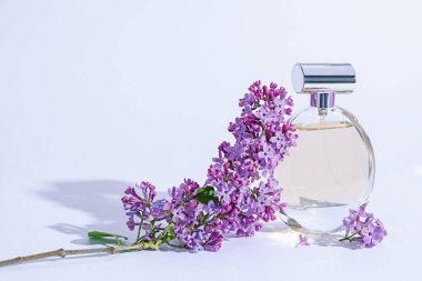 Parfüm şişesi ve dalında açık gri arka planda leylak çiçekleri, yakın plan.