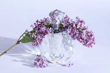 Parfüm şişesi ve dalında açık gri arka planda leylak çiçekleri, yakın plan.