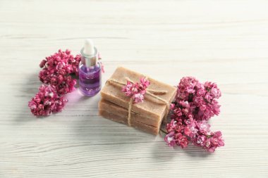 Bir yığın sabun, temel yağ ve açık ahşap masa üzerinde leylak çiçekleri.