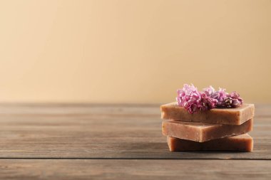 Ahşap masada bej arka planda duran bir yığın sabun ve leylak çiçeği, yakın plan. Metin için boşluk