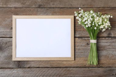 Bir buket güzel vadi zambağı ve ahşap arka planda boş çerçeve, üst manzara. Metin için boşluk