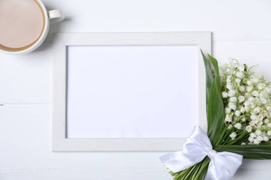 Bir buket güzel vadi zambağı çiçekleri, beyaz ahşap arka planda kahve ve boş çerçeve, düzlük. Metin için boşluk