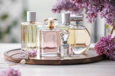 Beyaz ahşap masada, parfüm şişeleri ve leylak çiçekleri, yakın plan.