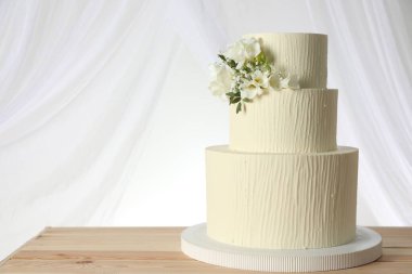 Ahşap masadaki çiçek desenli nefis düğün pastası ve beyaz arka plandaki perdeler.