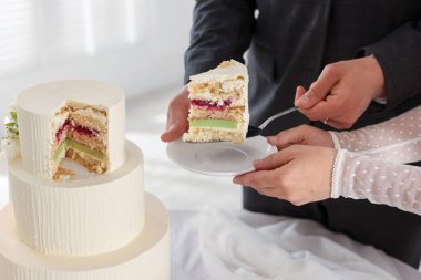 Damat, düğün pastasından bir parça tabağa koyuyor. Gelini masada kapalı tutuyor, yakın plan.