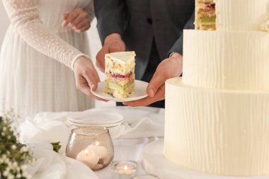 Yeni evliler, bir parça düğün pastasıyla tabağı evin içindeki masaya koyuyorlar.