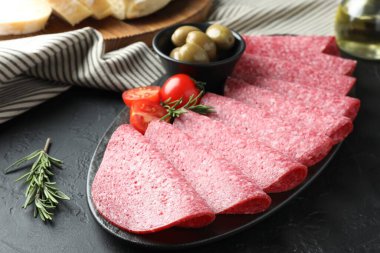 Siyah masada servis edilen zeytinli ve domatesli leziz sosis dilimleri.