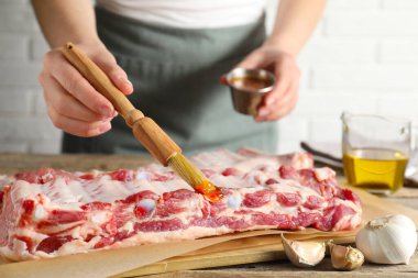 Kadın, masadaki çiğ domuz pirzolasına terbiye koyuyor.