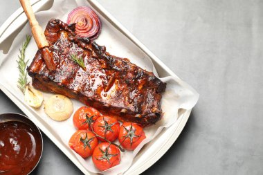 Lezzetli kaburgalar, biberiye, fırında soğan, sos ve gri masada kurutulmuş domatesler. Metin için boşluk