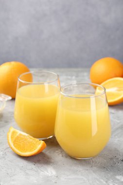 Bardakta portakal suyu ve gri masada taze meyve, yakın plan.