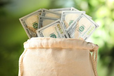 Bulanık yeşil arka planda dolar banknotları olan para çantası, yakın plan.