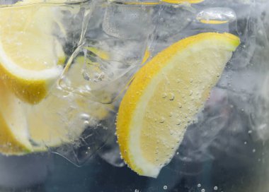 Koyu arkaplanda limon dilimleri ve buzla soda tazeleniyor. Yakın plan.