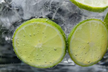 Koyu arkaplanda limon dilimleri ve buzla soda tazeleniyor. Yakın plan.