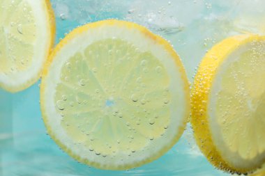 Açık mavi arka planda limon dilimleri ve buzla soda tazeleniyor. Yakın plan.