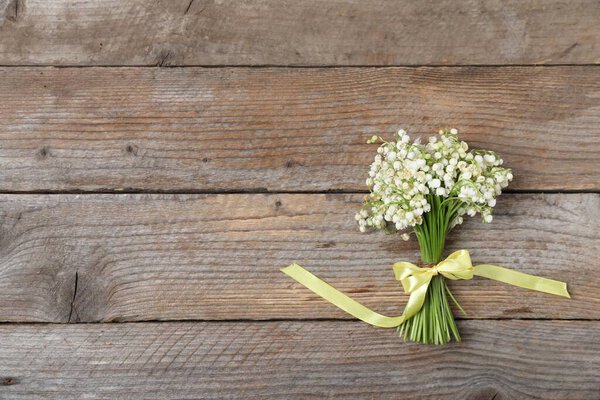 Букет красивых цветов из долины на деревянном фоне, вид сверху. Пространство для текста