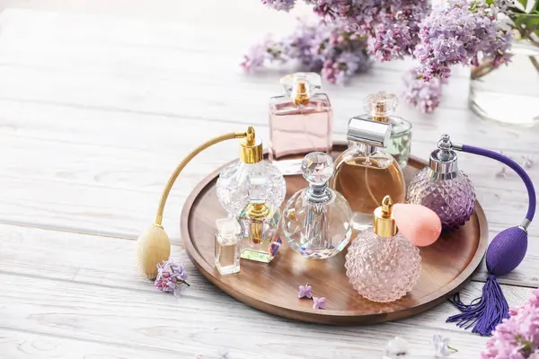 Beyaz ahşap masada parfüm şişeleri ve leylak çiçekleri. Metin için boşluk