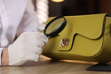 Kapalı bir masada deri çanta değerlendirmesi yapan büyüteçle bir eksper.