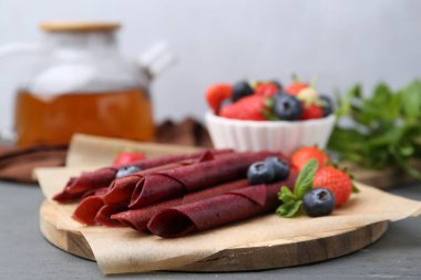 Lezzetli meyve dürümleri, çilekler, yaban mersinleri ve nane şekeri gri ahşap masada, yakın plan.