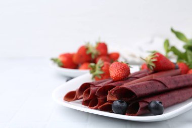 Lezzetli meyve dürümleri, çilekler ve yaban mersinleri beyaz masada, yakın plan. Metin için boşluk