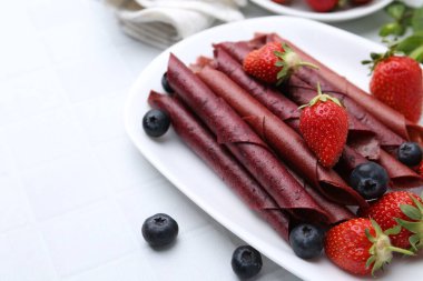 Lezzetli meyve dürümleri, çilekler ve yaban mersinleri beyaz masada, yakın plan. Metin için boşluk