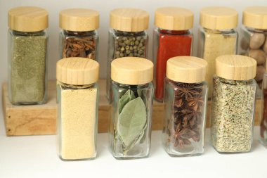 Beyaz masadaki kavanozlardaki farklı aromatik baharatlar, yakın plan.
