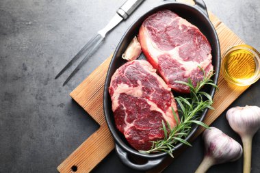 Fırın kabında baharatlı çiğ et parçaları, gri desenli masa üzerinde yağ ve çatal, düz yatar.